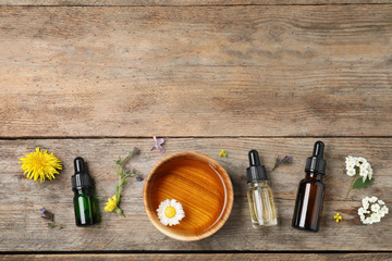 Flat lay composition with essential oils, bowl and flowers on wooden table, space for text