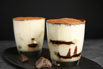 Two glasses of tiramisu cake on table against dark background, closeup