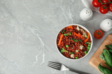 Bowl of brown rice with vegetables on grey table, flat lay. Space for text