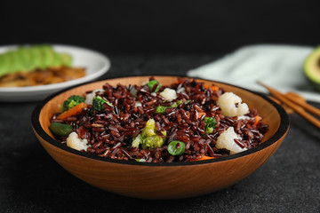 Plate of brown rice with vegetables on black table, closeup