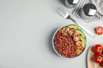 Bowl of brown rice with mushrooms and avocado on table, flat lay. Space for text