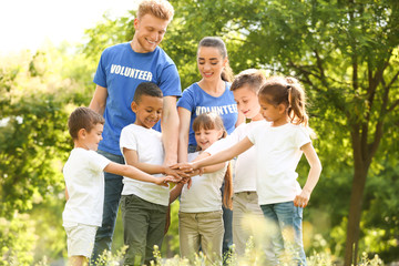 Group of kids joining hands with volunteers in park