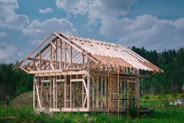 The erection of a wooden frame house. Modern wooden-frame country house under construction. Construction of the roof of a residential house. Unfinished house at construction site.
