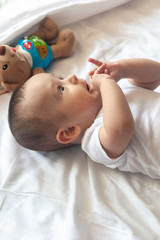 6-8-month-old baby boy lying playfully in bed. Charming 6-7 month little baby in white bodysuit. Baby boy in white bedding. Copy space