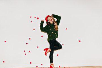 Full-length portrait of happy slim girl in black pants standing on one leg. Joyful caucasian lady wears red beret having fun in valentine's day in studio.