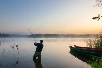 angler standing in the lake and catching the fish during misty dawn