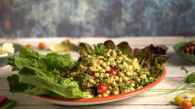 Closeup turning slide shot to left of beautiful platter of tabbouleh garnished with lettuce set against a blue background.