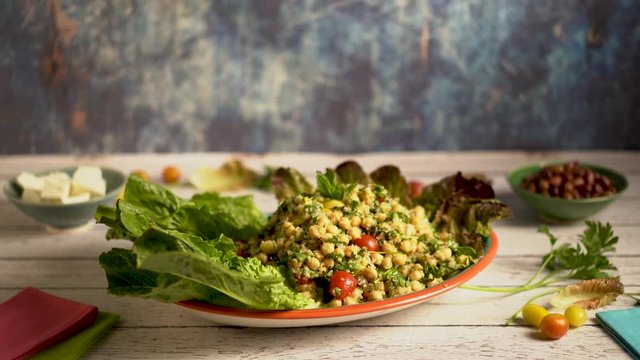 Turning slide shot of beautiful platter of tabbouleh garnished with lettuce set against a blue background.