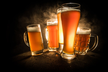 Creative concept. Beer glasses on wooden table at dark toned foggy background.