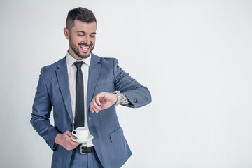 I should be there in time. Smiling businessman looking on his wrist watch and holds his coffe isolated on a white background the left space for your logo or text.