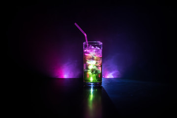 Cocktail glass splashing on dark toned smoky background or colorful cocktail in glass. Party club entertainment. Mixed light.