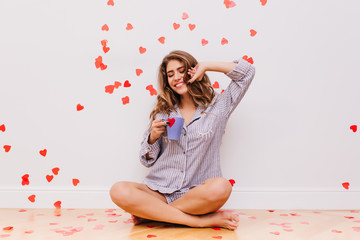 Barefooted pleasant woman sitting on the floor and drinking tea. Indoor shot of enthusiastic girl...