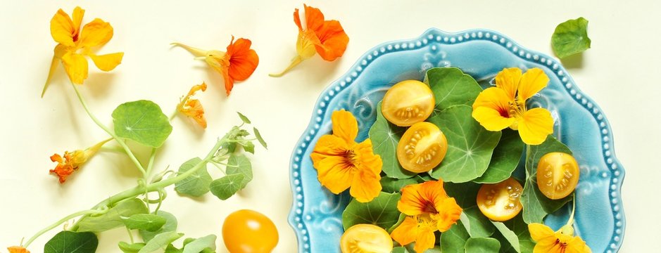 salad with nasturtium leaves and flowers of the plant. bright summer salad with edible yellow flowers and yellow tomatoes with egg. top view.