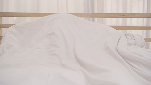 Asian couple lying on bed in bedroom, couple feeling happy having funny time playing under blanket together on bed at home. Couple relax enjoy love moment at home concept.