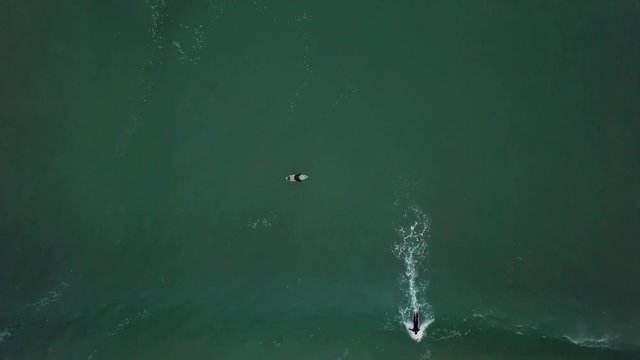 Pull away-shot of a surfer catching wave and leaving the frame. Birds-eye-view drone-shot.