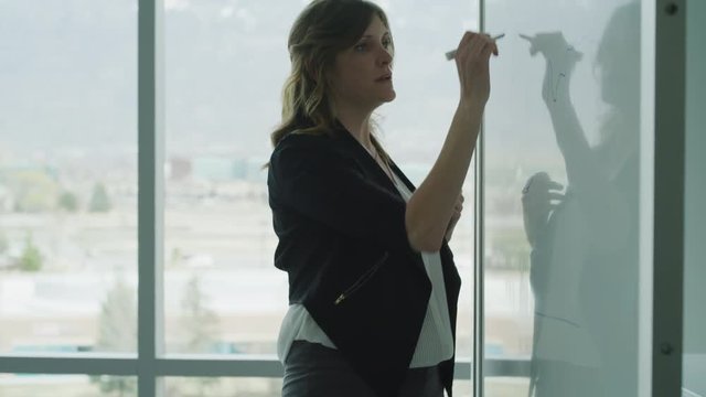 Tilt up to businesswoman talking and writing on whiteboard near window / Pleasant Grove, Utah, United States