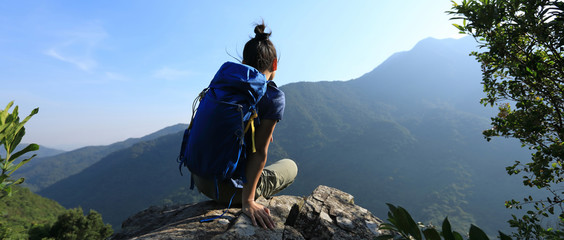 Successful woman backpacker sit on cliff's edge at mountain top