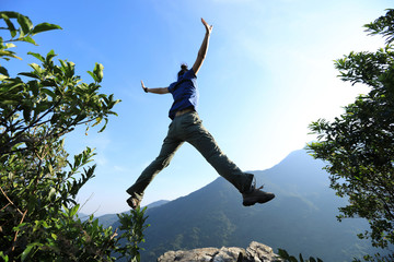Successful young woman hiker jumping on cliff's edge at mountain top