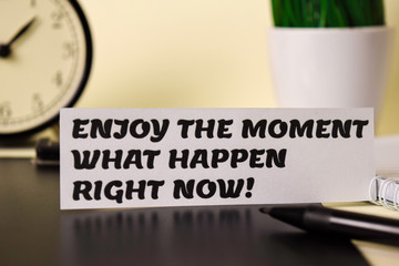 Fototapeta premium Enjoy The Moment What Happen Right Now! on the paper isolated on it desk. Business and inspiration concept