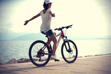 Fototapeta premium Woman riding a bike on sunny seaside with arms outstretched