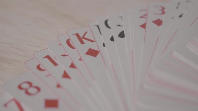 Playing cards in white and red, on a table. Image is in close up and blurred background.