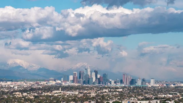 Time lapse of storm clouds racing over downtown Los Angeles with snow-capped mountains in background.