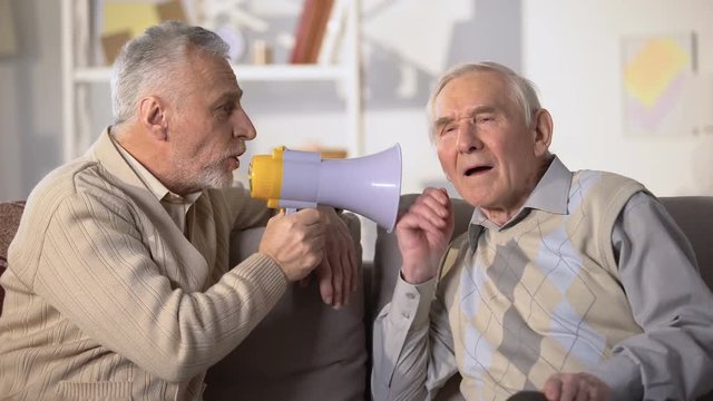 Elderly male talking in megaphone to deaf old friend, health problems, close-up