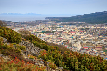 View of the city of Magadan from the mountainside. Cityscape with streets and buildings. Magadan is surrounded by beautiful nature. Sea bay in the distance. Magadan Region, Far East of Russia. Siberia