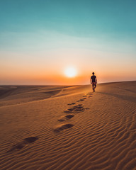 Fototapeta na wymiar Man walking alone in the dunes of the desert
