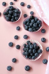 Blueberry berries. Blueberry muffins. Large blueberries in muffin tins and a pink towel on a  pink pastel background. Blueberry season. Berry baking concept.