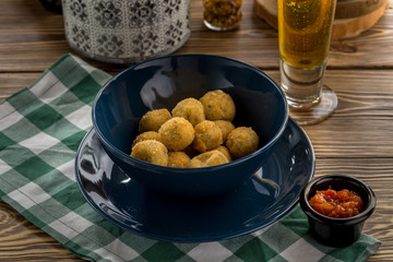 Fried potato cheese balls or croquettes with tomato ketchup and glass of beer on wooden table