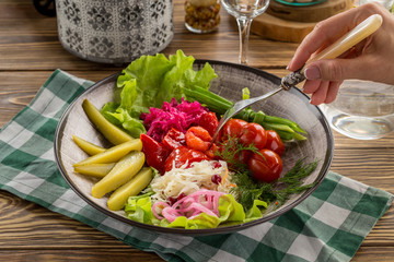 female hand with fork picking up pickled vegetables from plate on wooden table