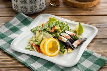 Fresh green salad with salmon cream cheese sushi on the side on wooden table