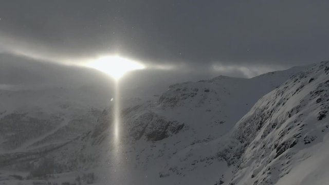 Snowy mountains in low light through clouds while snowing. Wide shot. Drone moving up