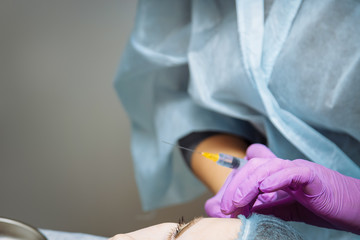 Fototapeta premium Beautiful young woman is getting a rejuvenating facial injections. The beautician is filling female wrinkles by hyaluronic acid. Young woman in a beauty salon. Cosmetology skin care.