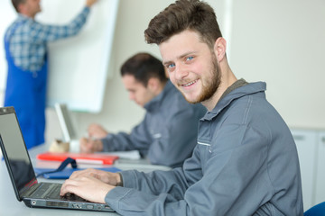 portrait of young man wearing overalls using laptop