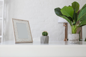 White office desk in a white room. On the table is a photo frame and green plants.