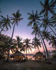 Two tents in a desert island with palm trees by sunset