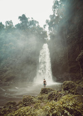 Guy alone in the middle of a huge waterfall in Bali, Indonesia