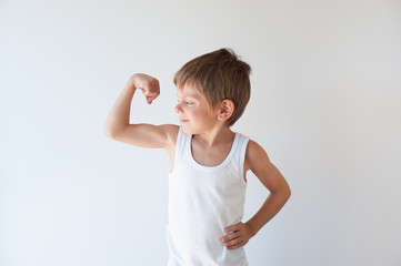 strong little caucasian boy in white tank top showing muscles with smile on his face