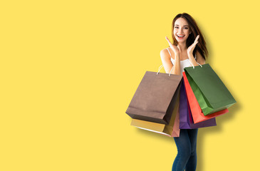 Happy excited girl in summer casual smart clothing, holding shopping bags, isolated over yellow...