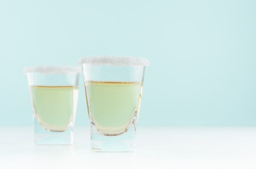 Exotic coctail with sour green lime in shot glass with sugar rim on soft light mint color...