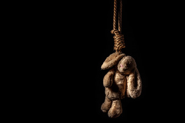 Rabbit toy, hanged on a thick braided rope on a dark background. Suicide conception.
