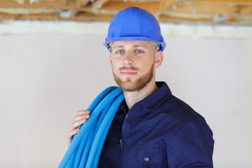 builder with reel of blue pipe over his shoulder