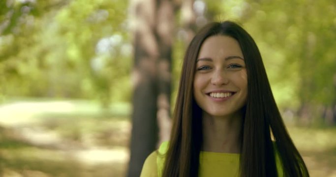 joyful pretty brunette girl is smiling broadly and playing jokingly with hair in summer day