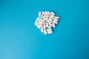 A small pile of white and pill capsules lies on a blue background.
