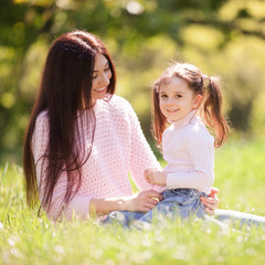 Happy mother and daughter in the summer park. Beauty nature scene with family outdoor lifestyle. Happy family resting together on green grass, having fun outdoor. Happiness and harmony in family life