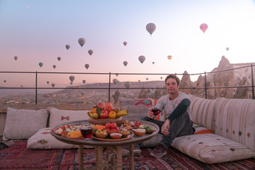Young white guy having breakfast in Capadoccia with many ballons in background - obrazy, fototapety, plakaty