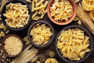 Variety of types and sshapes of dry Italian pasta in bowls against dark rustic wooden background