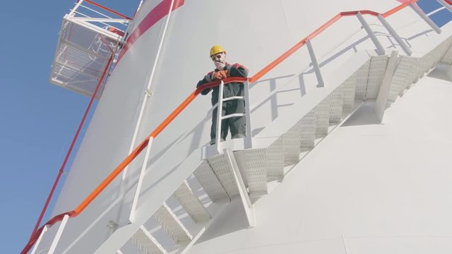 Petrochemical engineer stands on fuel tank ladder and commands via transmitter